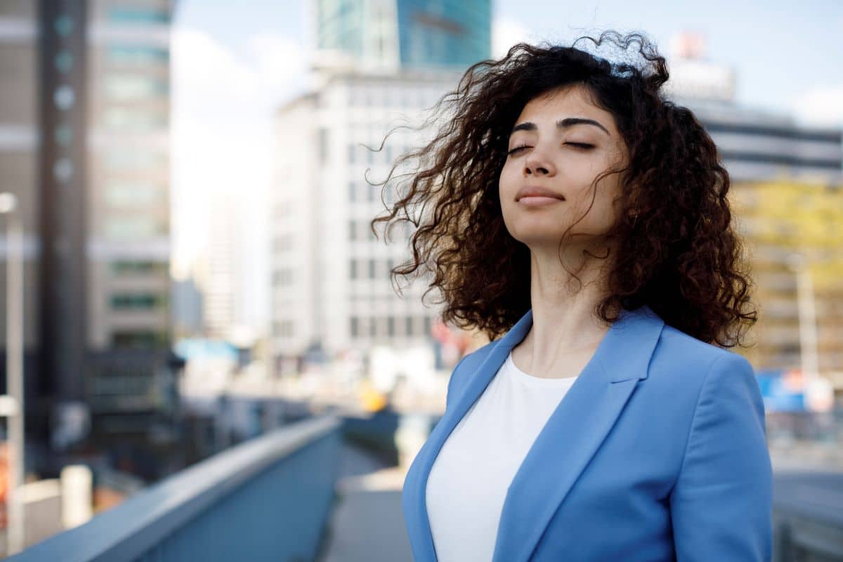 women experiencing Nasal Congestion Blockage younger woman in an outdoor cityscape closing her eyes as the wind blows her hair forward